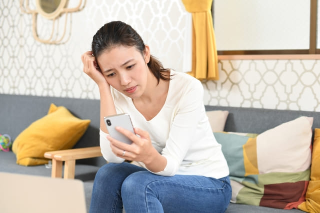部屋の中で、携帯のメッセージを見て考え込む女性。